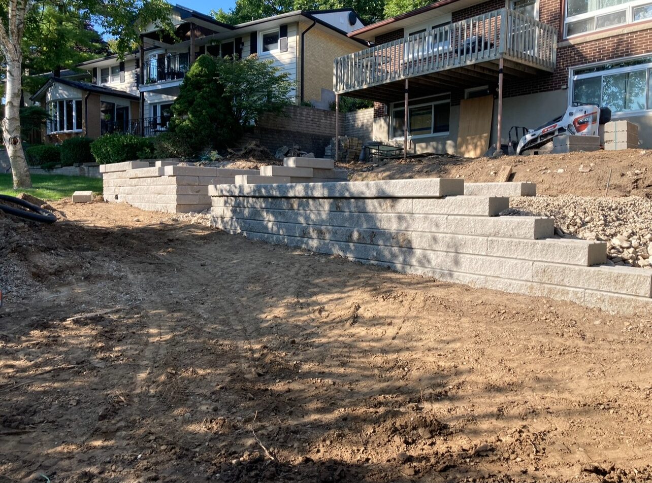 A residential area undergoing construction, featuring tiered retaining walls and houses with balconies. No recognizable landmarks or historical buildings are present.