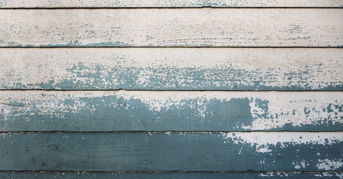 Weathered wooden wall with peeling blue and white paint, showcasing a rustic, aged texture and horizontal lines creating a vintage, coastal aesthetic.