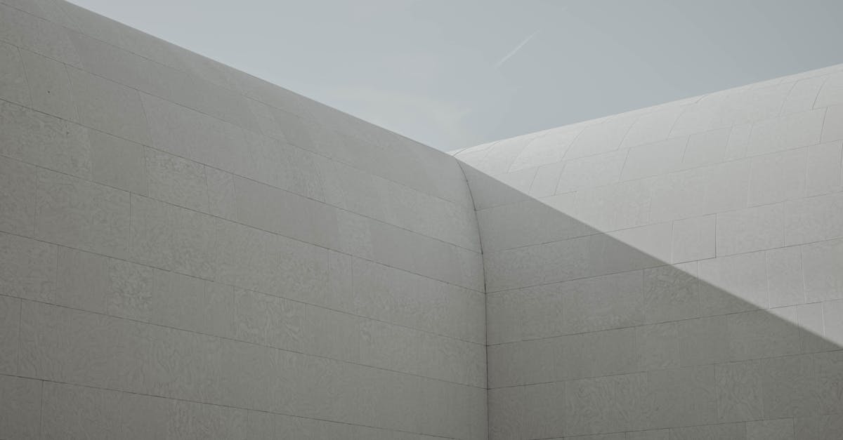 Modern architectural structure with smooth, curved concrete walls and clear sky, showcasing minimalist design and geometric shadows on the surface.