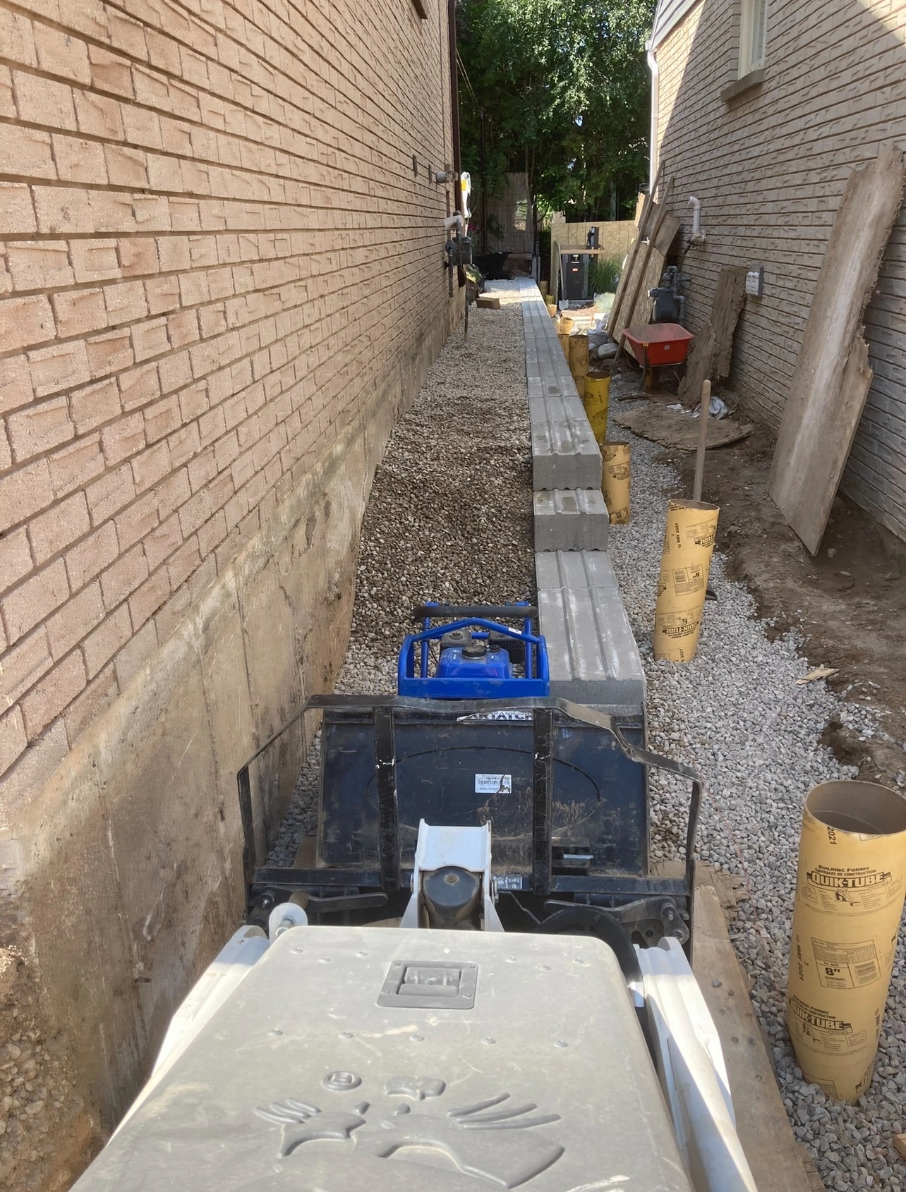 A narrow alley between brick buildings with construction materials, equipment, and gravel, where a person works in the background.