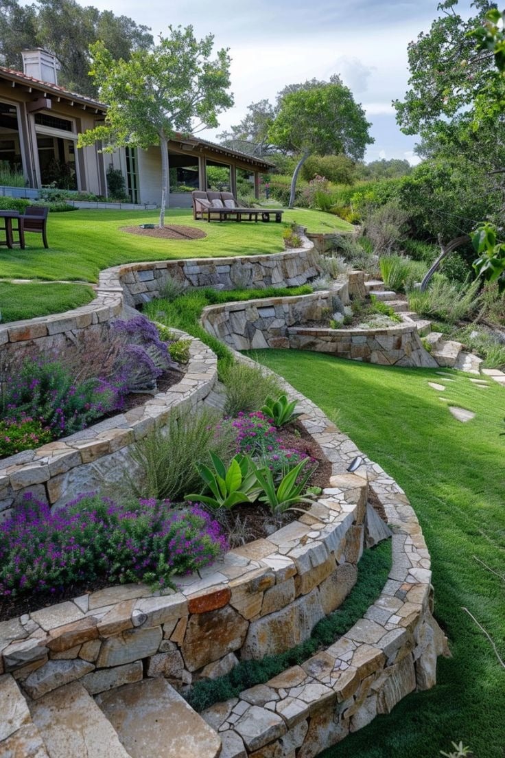 Terraced garden with vibrant flowers, stone walls, and lush greenery. A person enjoys the scenic view from a modern house's patio.